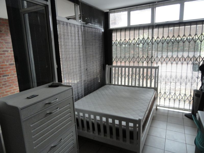 A bedroom featuring tiled flooring, large windows with security gates, and natural light, offering a functional space ready for personal touches.