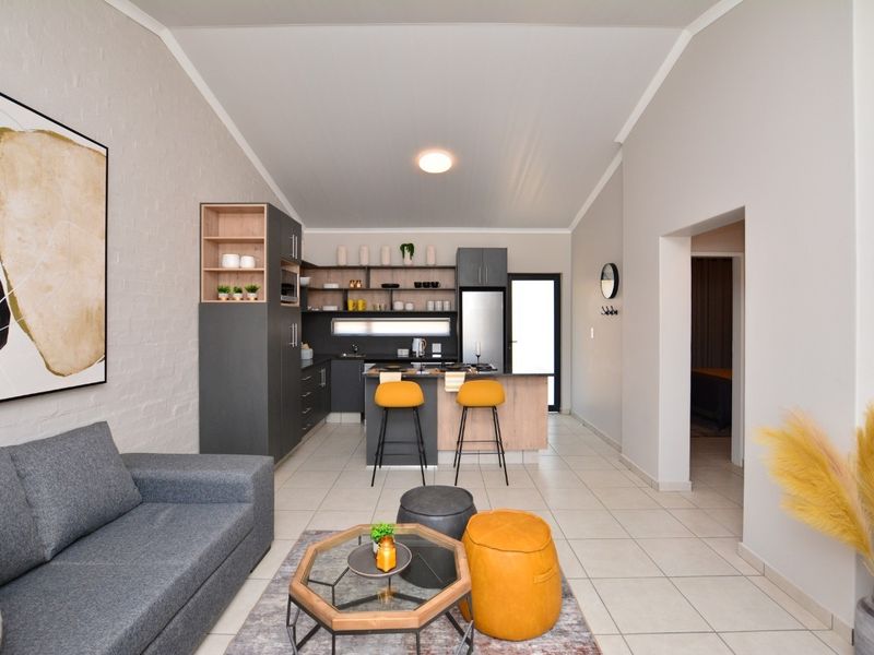 Modern open-plan living area featuring a contemporary kitchen with built-in cabinetry, a central island, and high vaulted ceilings with tiled flooring throughout.