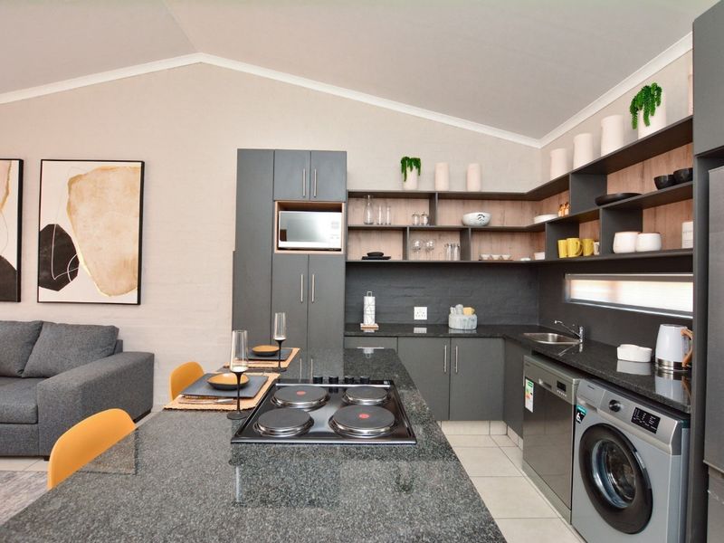 Modern open-plan kitchen featuring dark cabinetry, granite countertops, integrated appliances, and a central island with an electric hob, seamlessly flowing into the living area.