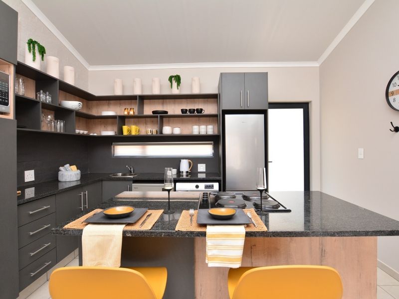 Modern kitchen featuring dark cabinetry, granite countertops, a central island with an integrated hob, and open shelving for storage.