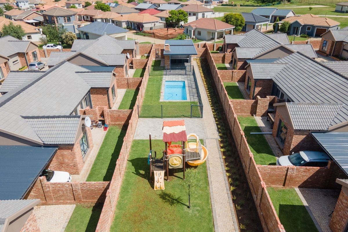 Aerial view of a residential townhouse complex featuring individual brick units, private gardens, paved pathways, and a communal swimming pool area.