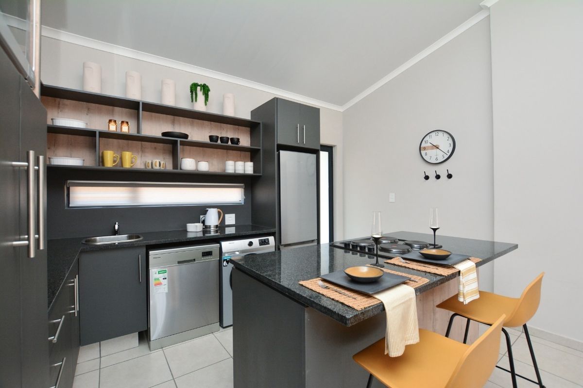 Modern kitchen featuring dark cabinetry, granite countertops, an integrated island with a built-in hob, and open shelving for storage.