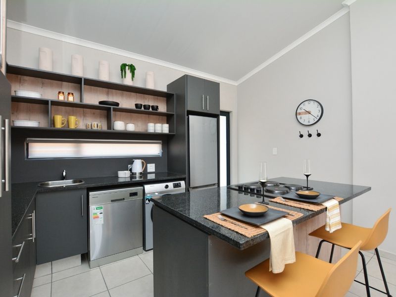 Modern kitchen featuring dark cabinetry, granite countertops, an integrated island with a built-in hob, and open shelving for storage.