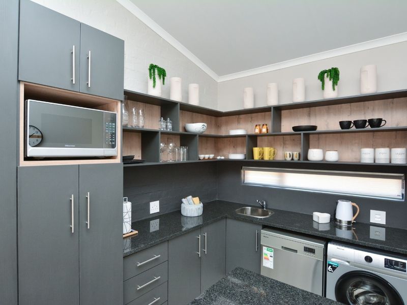 Modern scullery featuring dark grey cabinetry, granite countertops, open shelving, and integrated appliance connections for a dishwasher and washing machine.