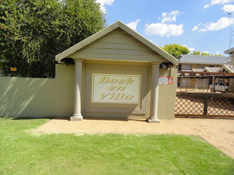 The entrance to Boek en Villa apartment complex featuring a secure gated access point, paved driveway, and decorative pillars.