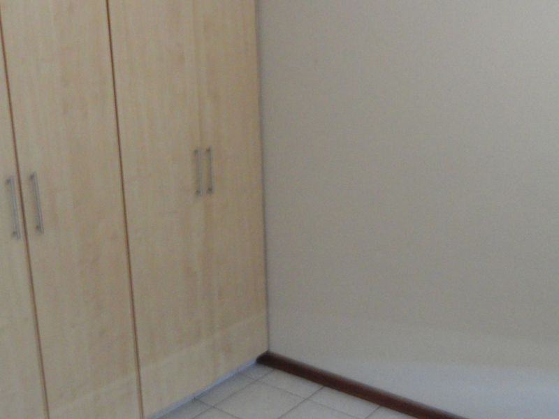 A bedroom interior featuring light wood-finish built-in cupboards, tiled flooring, and neutral wall tones.