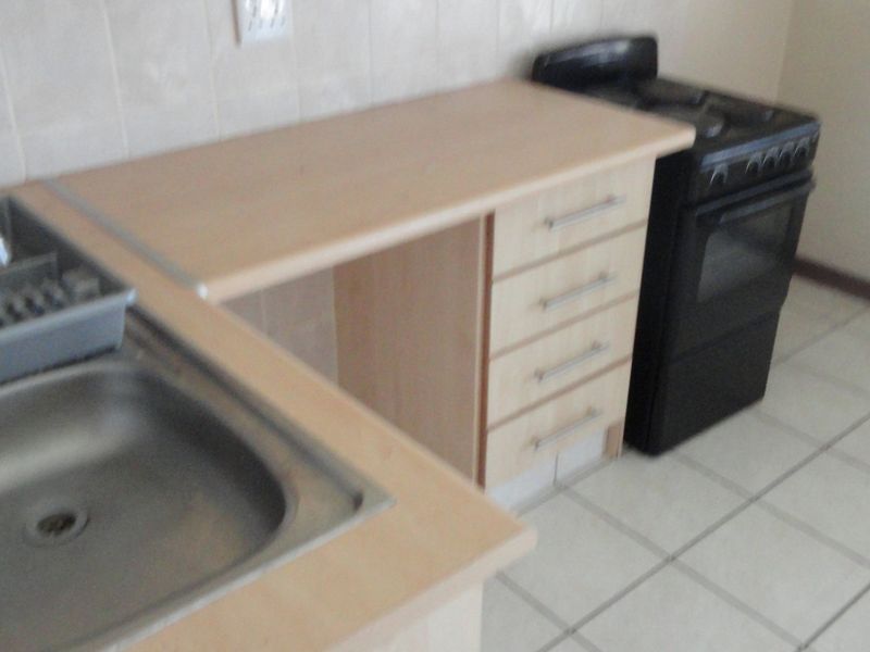 A functional kitchen area featuring a stainless steel sink, laminate countertops, built-in cabinetry, and a freestanding oven with tiled flooring.
