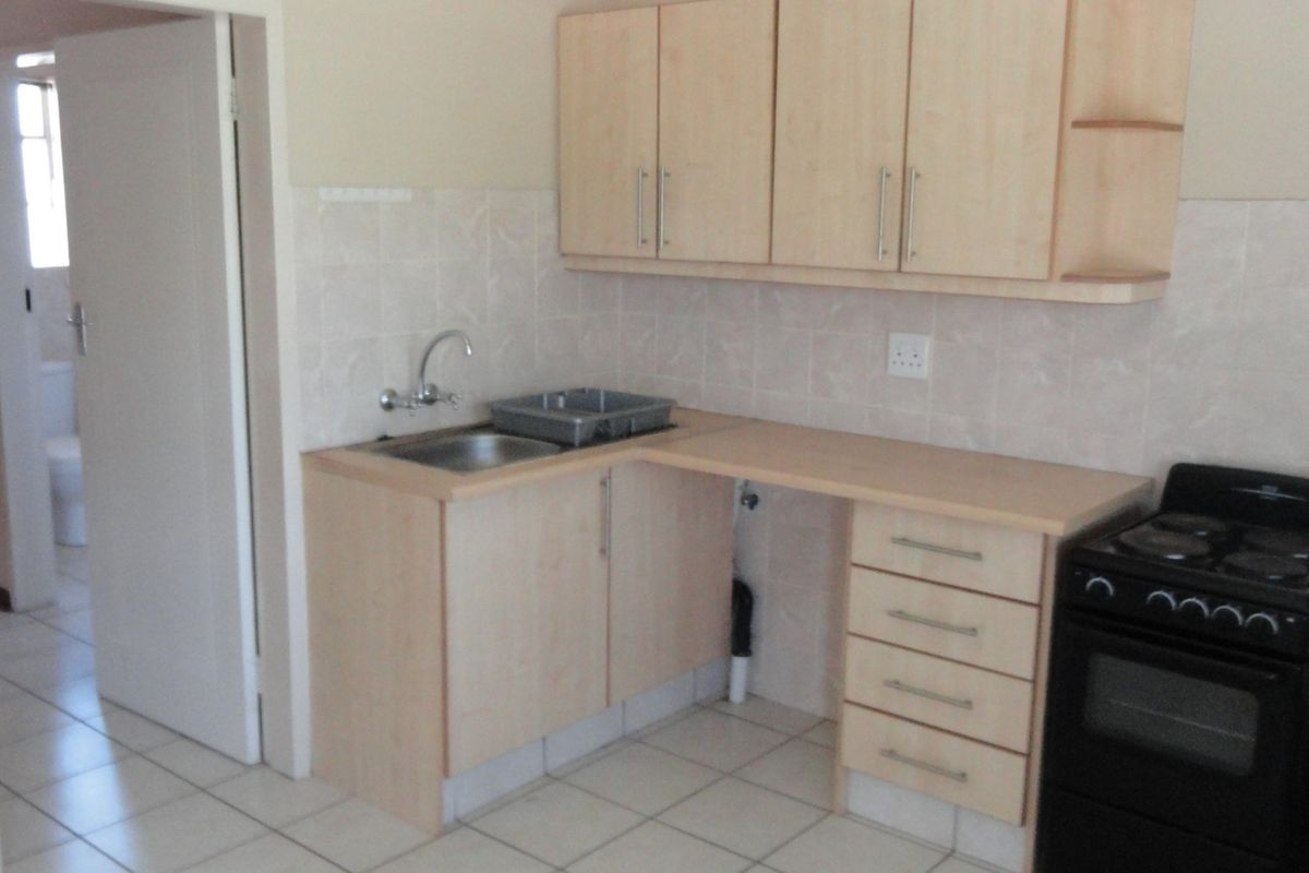 A functional kitchen featuring light laminate cabinetry, tiled backsplash, stainless steel sink, and a freestanding stove with tiled flooring throughout.