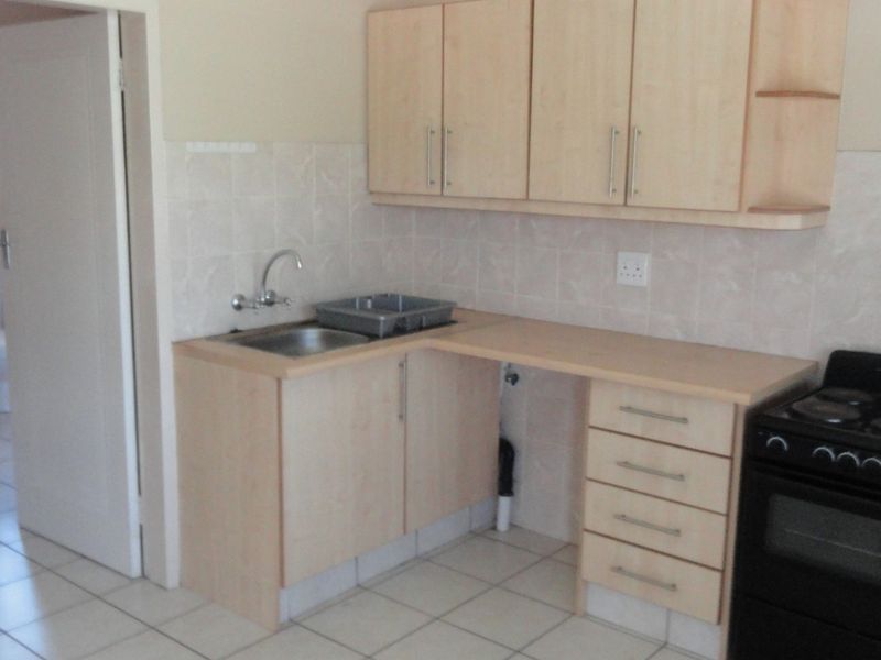 A functional kitchen featuring light laminate cabinetry, tiled backsplash, stainless steel sink, and a freestanding stove with tiled flooring throughout.
