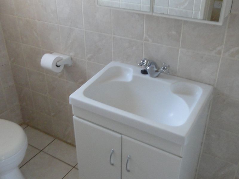 A functional bathroom featuring a white vanity cabinet with a basin, a standard toilet, and neutral wall and floor tiling.