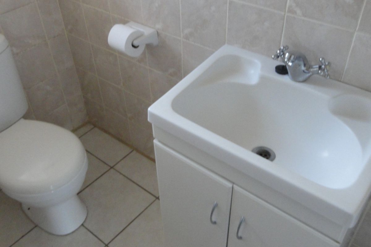 A functional bathroom featuring a white vanity cabinet with integrated basin, standard toilet, and neutral wall and floor tiling.