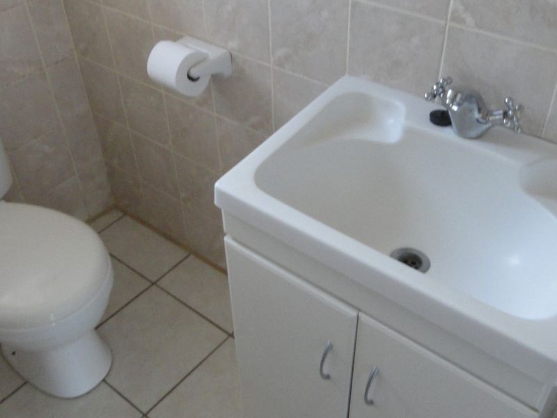 A functional bathroom featuring a white vanity cabinet with integrated basin, standard toilet, and neutral wall and floor tiling.