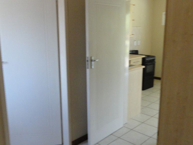 A hallway area featuring tiled flooring and built-in cupboards, providing access to adjacent rooms including a kitchen area.