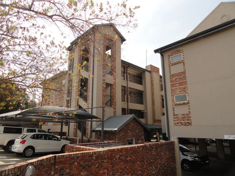 Exterior view of a multi-story apartment complex featuring brick detailing, covered parking bays, and a central stairwell tower.