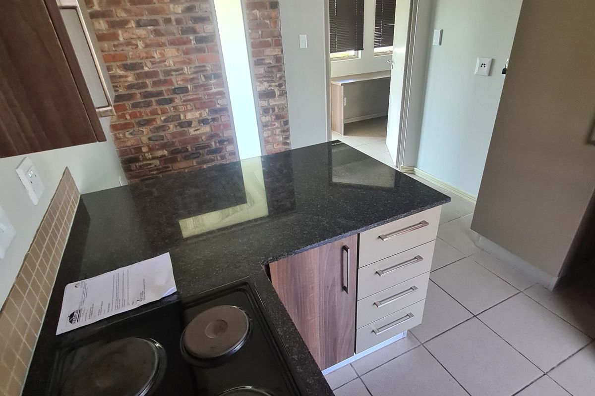 A functional kitchen featuring granite countertops, an electric hob, built-in cabinetry, and a distinctive exposed brick feature wall with tiled flooring.
