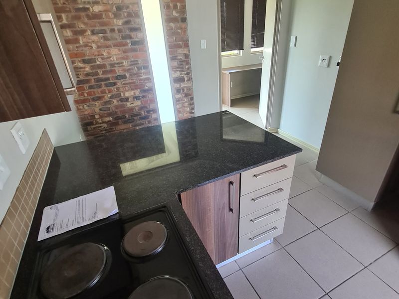 A functional kitchen featuring granite countertops, an electric hob, built-in cabinetry, and a distinctive exposed brick feature wall with tiled flooring.