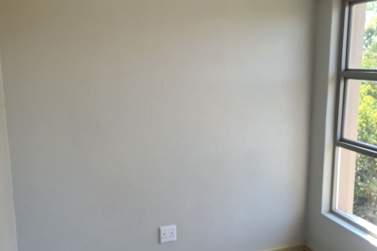 A vacant bedroom featuring neutral wall paint, tiled flooring, and a window with an aluminium frame, providing a clean canvas for personalization.