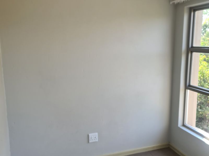 A vacant bedroom featuring neutral wall paint, tiled flooring, and a window with an aluminium frame, providing a clean canvas for personalization.