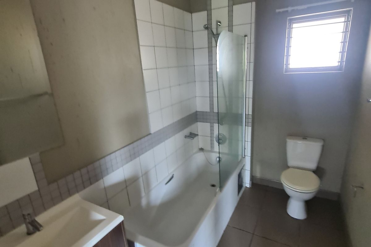 A functional bathroom featuring a vanity basin, bathtub with a glass shower screen, and a toilet, finished with tiled flooring and wall accents.