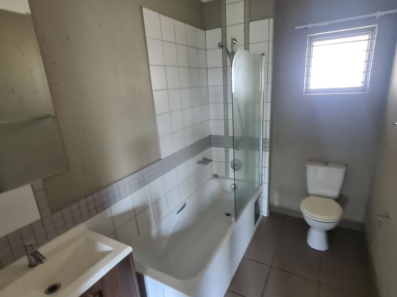 A functional bathroom featuring a vanity basin, bathtub with a glass shower screen, and a toilet, finished with tiled flooring and wall accents.