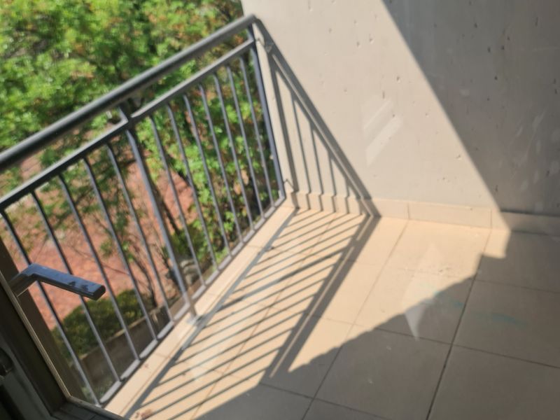 A compact balcony featuring tiled flooring and a metal balustrade, accessible via a sliding glass door, offering an outdoor space with a leafy outlook.