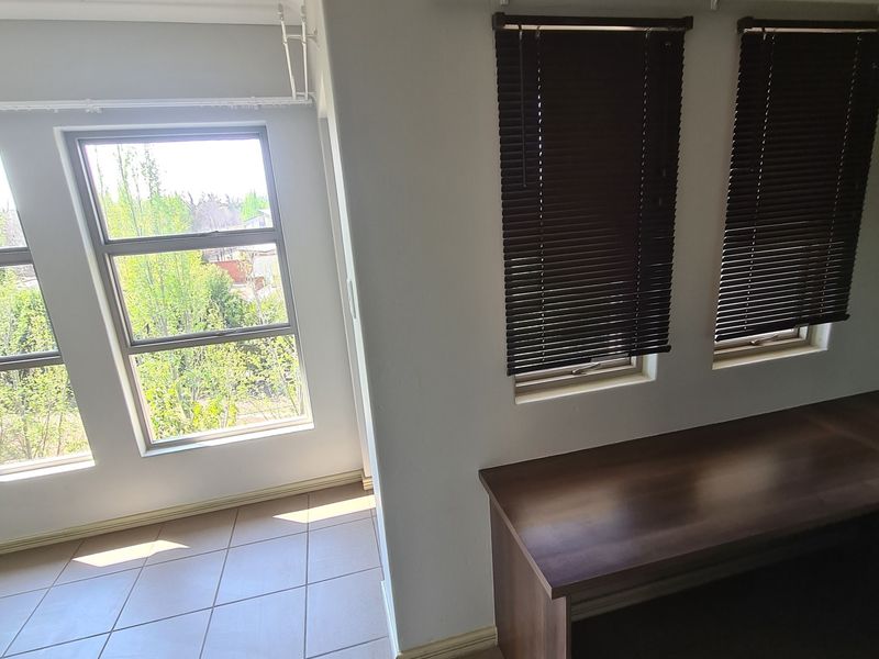 A bright, tiled office space featuring a built-in desk, venetian blinds, and large windows providing natural light and exterior views.