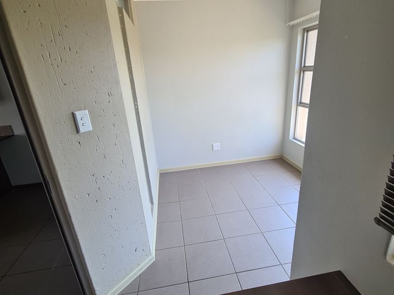 An empty bedroom featuring neutral tiled flooring, a window for natural light, and standard ceiling lighting.