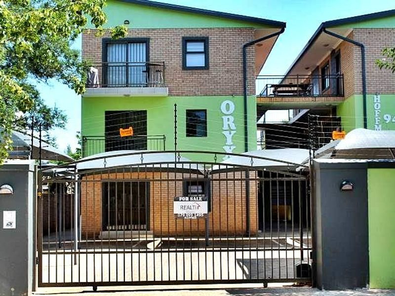 Front elevation of a multi-story apartment complex featuring brick and painted facade, secure gated entrance, electric fencing, and balcony access.