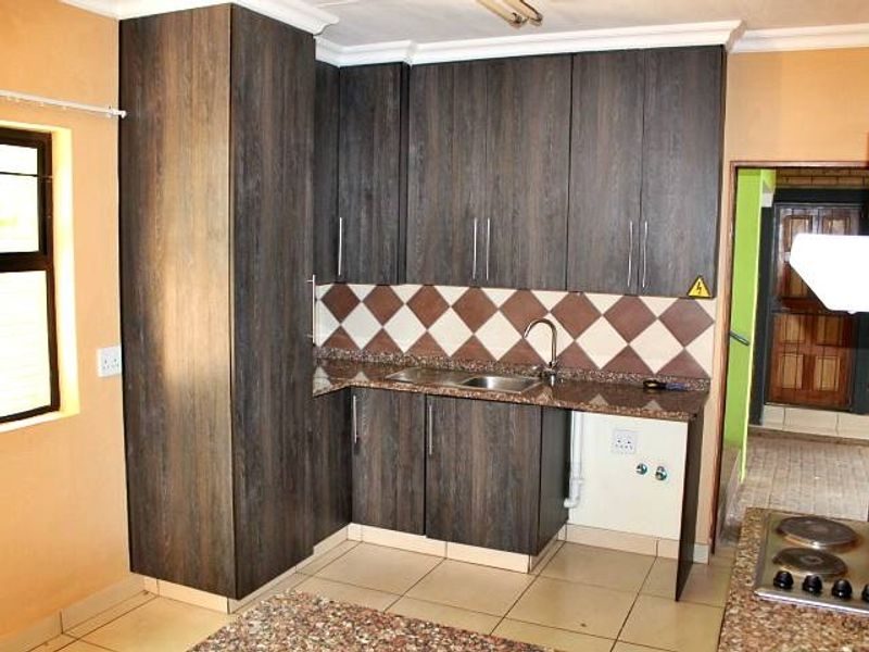 A functional kitchen featuring dark wood-grain cabinetry, granite countertops, a tiled backsplash, and ceramic floor tiles, offering a practical layout for culinary activities.