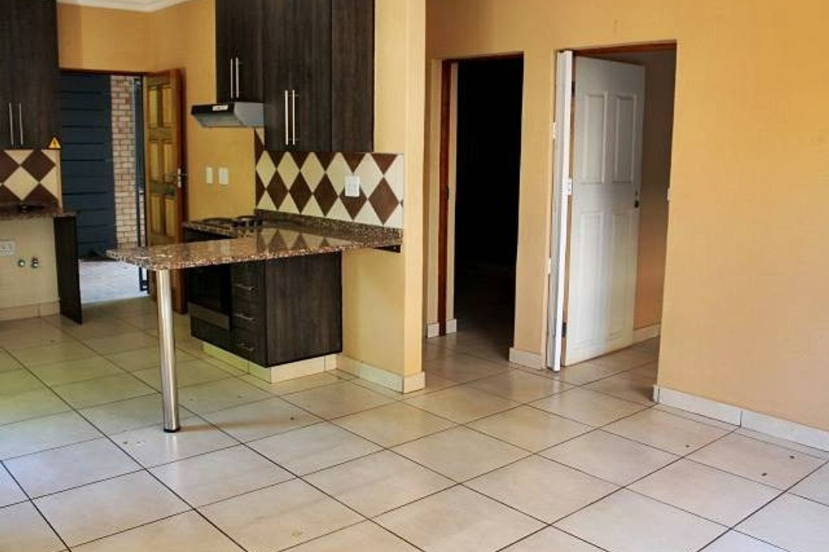 An open-plan kitchen featuring dark wood cabinetry, granite countertops with a breakfast bar, and tiled flooring, leading into adjacent living and hallway areas.