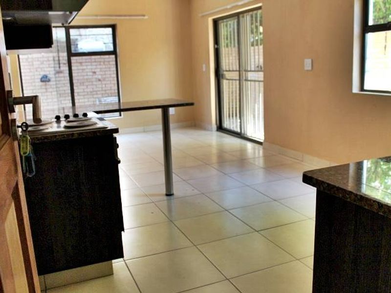 An open-plan kitchen and living area featuring tiled flooring, granite countertops, and a sliding glass door leading to the exterior.