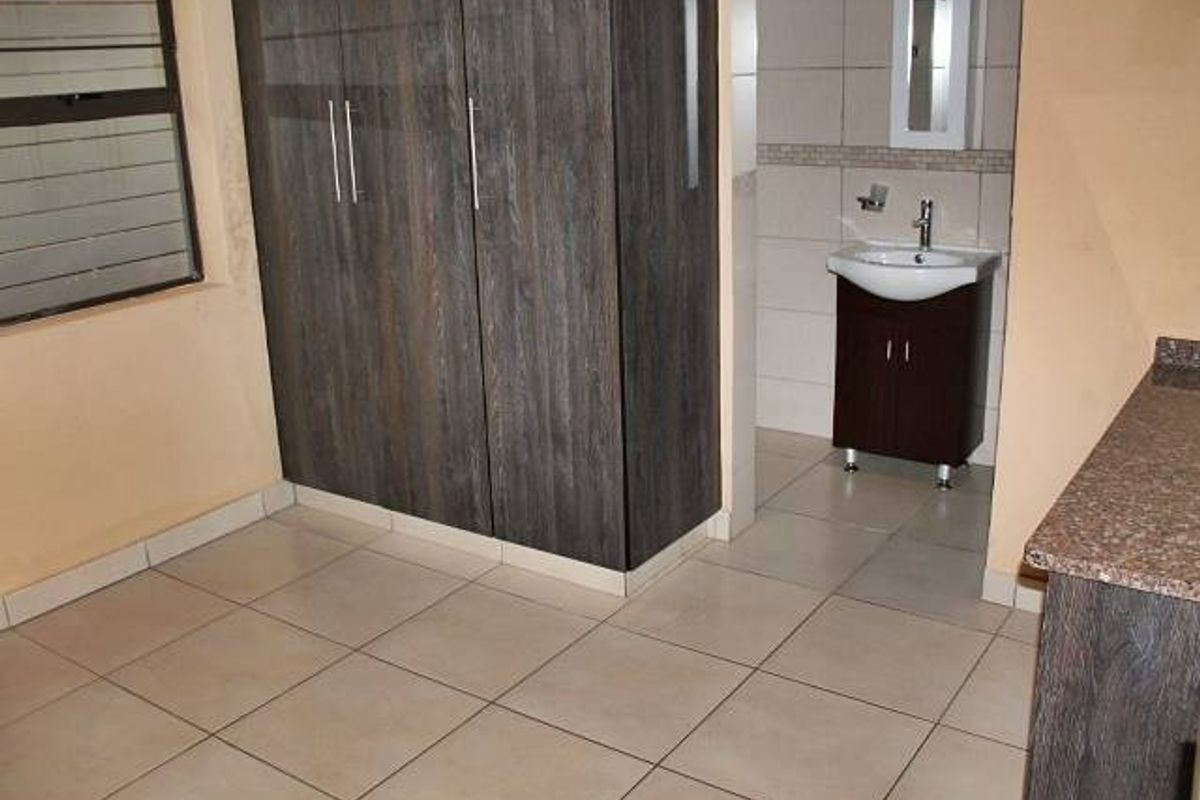 A bedroom featuring built-in cupboards and an en-suite vanity area with a basin and mirror cabinet, finished with neutral floor tiles.