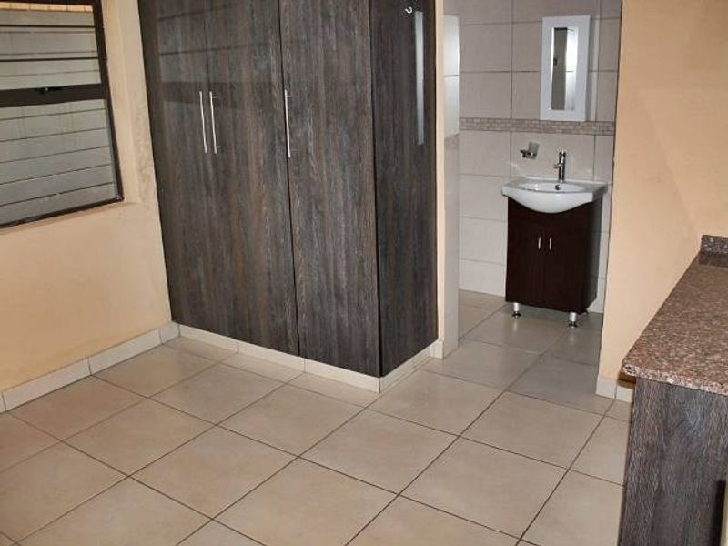 A bedroom featuring built-in cupboards and an en-suite vanity area with a basin and mirror cabinet, finished with neutral floor tiles.