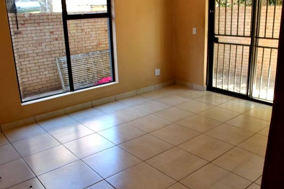 An empty living area featuring neutral floor tiles, large windows, and a sliding glass door with a security gate leading to the exterior.