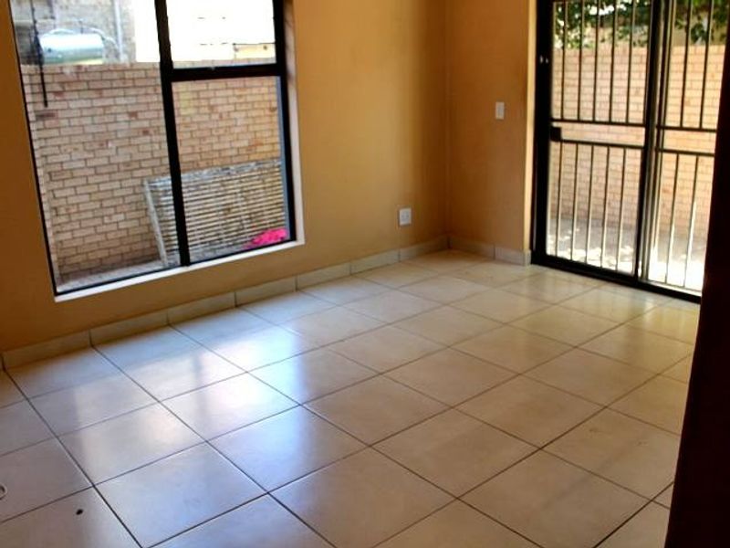 An empty living area featuring neutral floor tiles, large windows, and a sliding glass door with a security gate leading to the exterior.