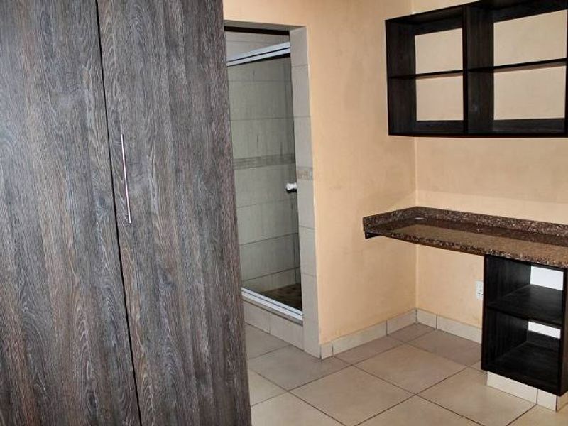 Bedroom featuring built-in wardrobe, integrated desk with shelving, tiled flooring, and an adjoining en-suite shower room.