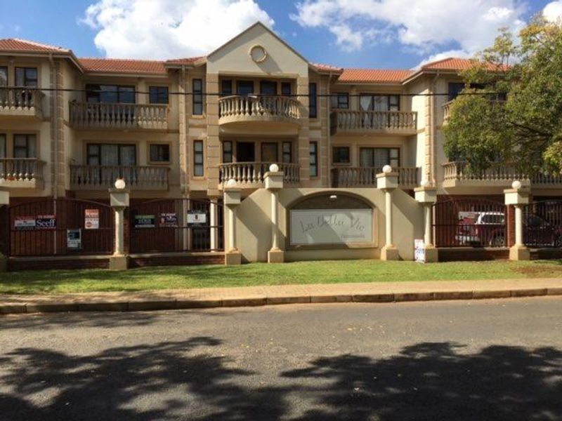 Front elevation of La Bella Vie apartment complex featuring multi-story residential units with private balconies, tiled roofing, and secure perimeter fencing.