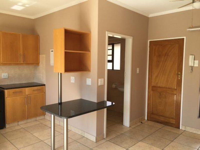 A functional kitchen area featuring built-in wooden cabinetry, a breakfast bar, and tiled flooring, with direct access to an adjacent room.