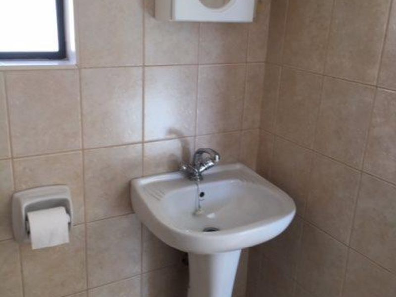 A functional bathroom featuring a pedestal basin, chrome mixer tap, and wall-mounted medicine cabinet, finished with neutral ceramic wall and floor tiles.