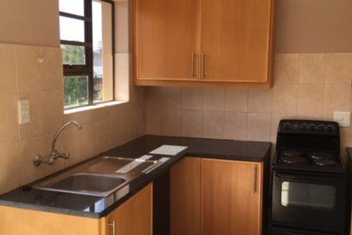 A functional kitchen featuring wooden cabinetry, laminate countertops, a stainless steel sink, and a freestanding stove with tiled backsplash and flooring.