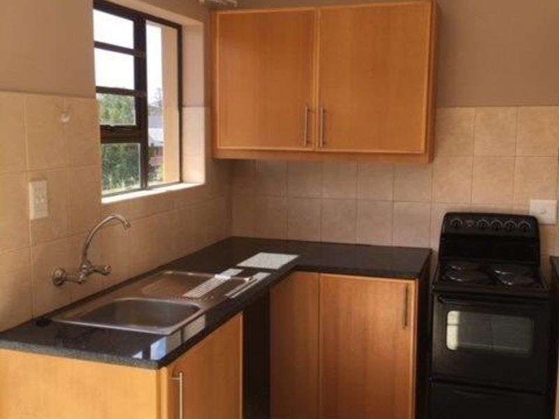 A functional kitchen featuring wooden cabinetry, laminate countertops, a stainless steel sink, and a freestanding stove with tiled backsplash and flooring.