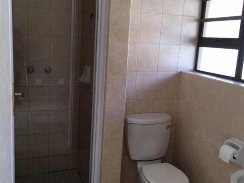 A functional bathroom featuring a tiled shower enclosure, a standard toilet, and neutral wall tiling with natural light from a side window.