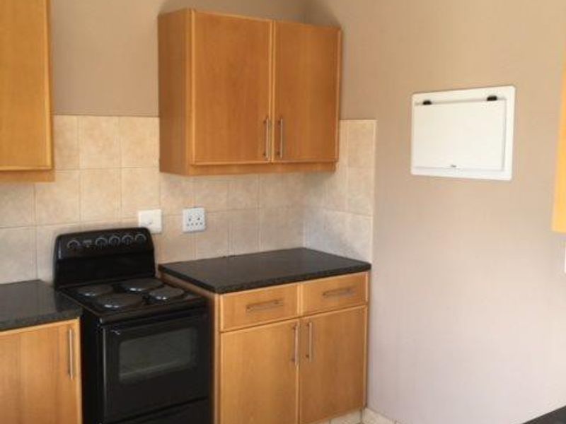 A functional kitchen featuring light wood-finish cabinetry, dark countertops, tiled backsplash, and a freestanding stove with ceramic floor tiles.