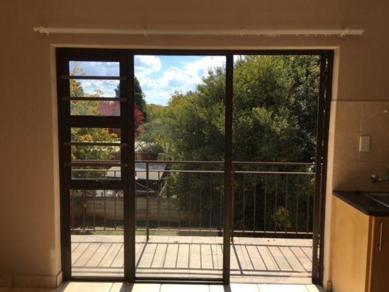 A view from an interior space through a sliding door onto a balcony with a metal balustrade and outdoor greenery.
