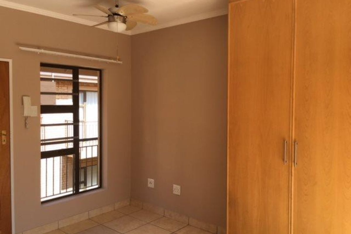 A clean, empty bedroom featuring tiled flooring, a built-in wooden wardrobe, and a ceiling fan, offering a neutral canvas for personalization.