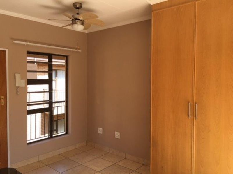 A clean, empty bedroom featuring tiled flooring, a built-in wooden wardrobe, and a ceiling fan, offering a neutral canvas for personalization.