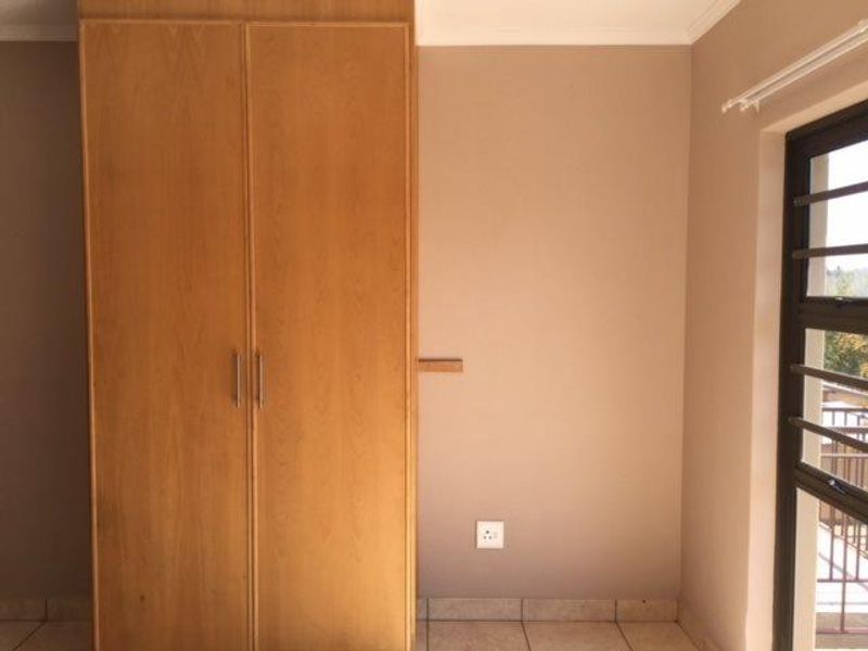 A clean, empty bedroom featuring a built-in wooden wardrobe, tiled flooring, and a window with security bars.