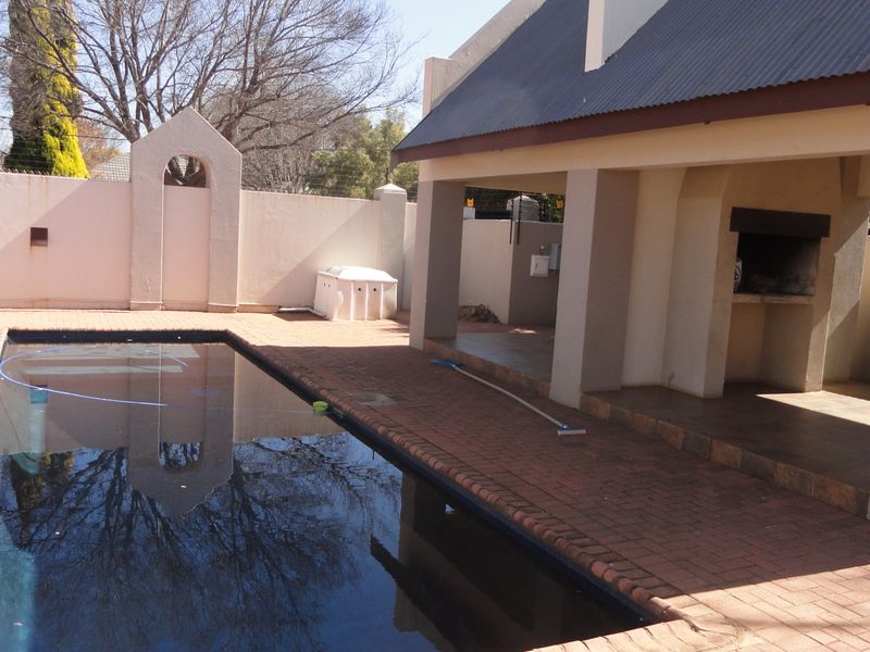 Outdoor entertainment area featuring a swimming pool and a covered patio with a built-in braai, set within a private walled garden.