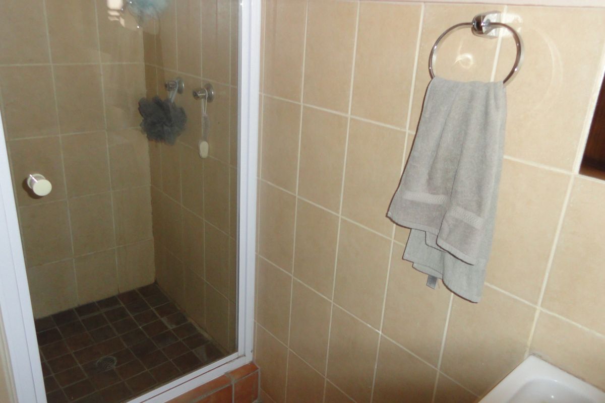 A functional bathroom featuring a shower enclosure with tiled walls and flooring, equipped with a wall-mounted towel ring.