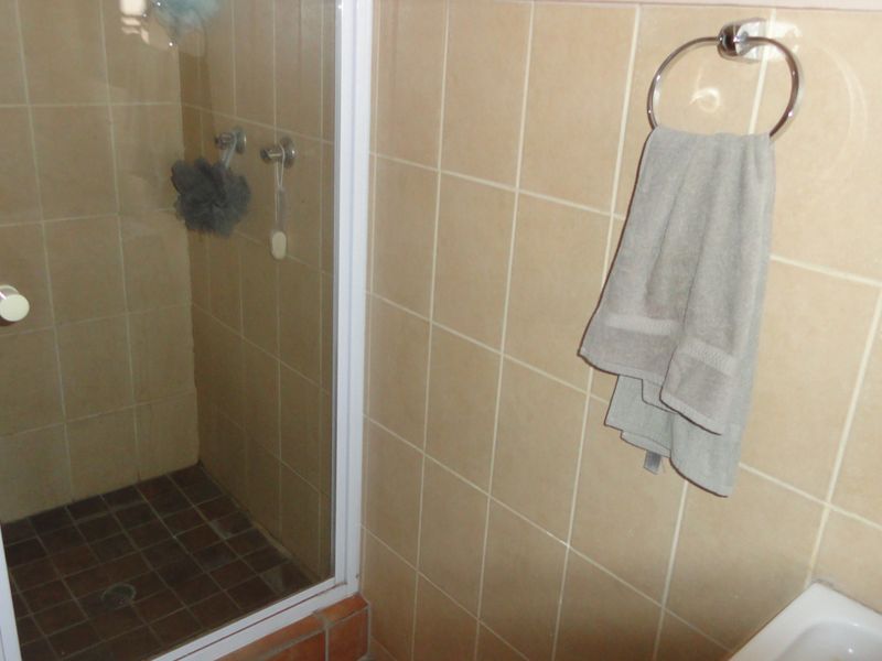 A functional bathroom featuring a shower enclosure with tiled walls and flooring, equipped with a wall-mounted towel ring.